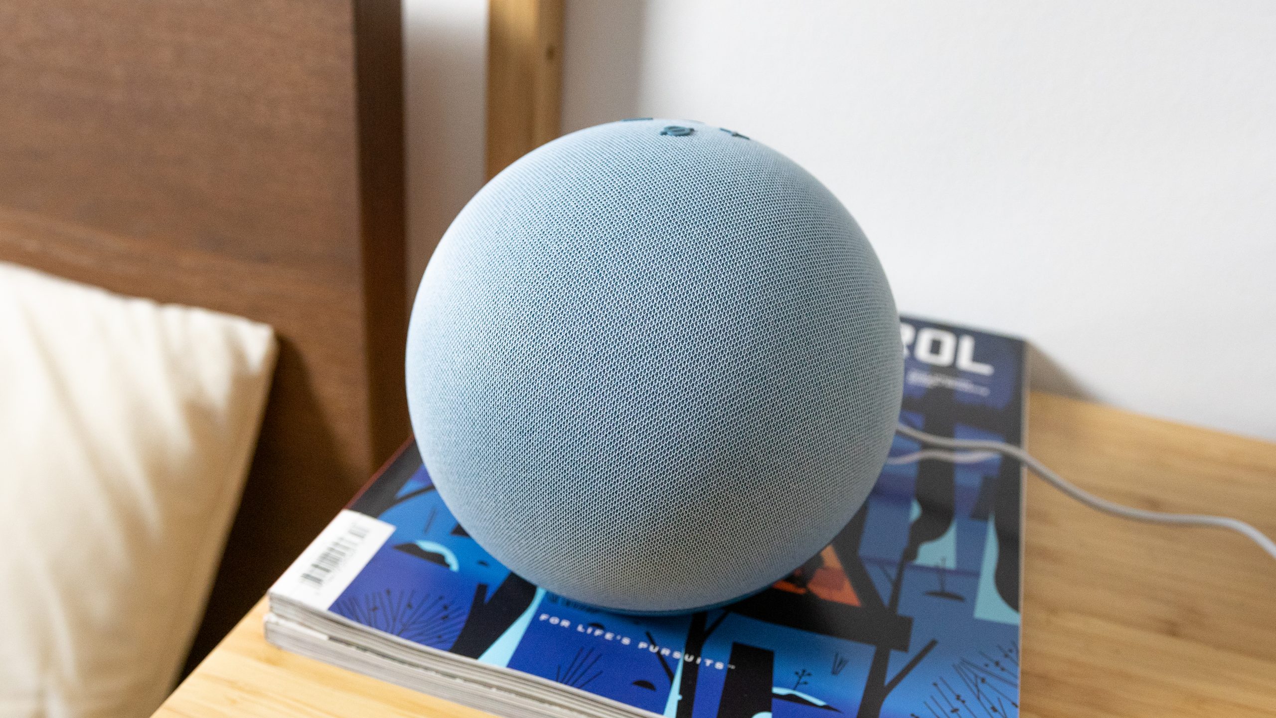 The Amazon Echo (4th gen.) on a bedside table with bed in the background.