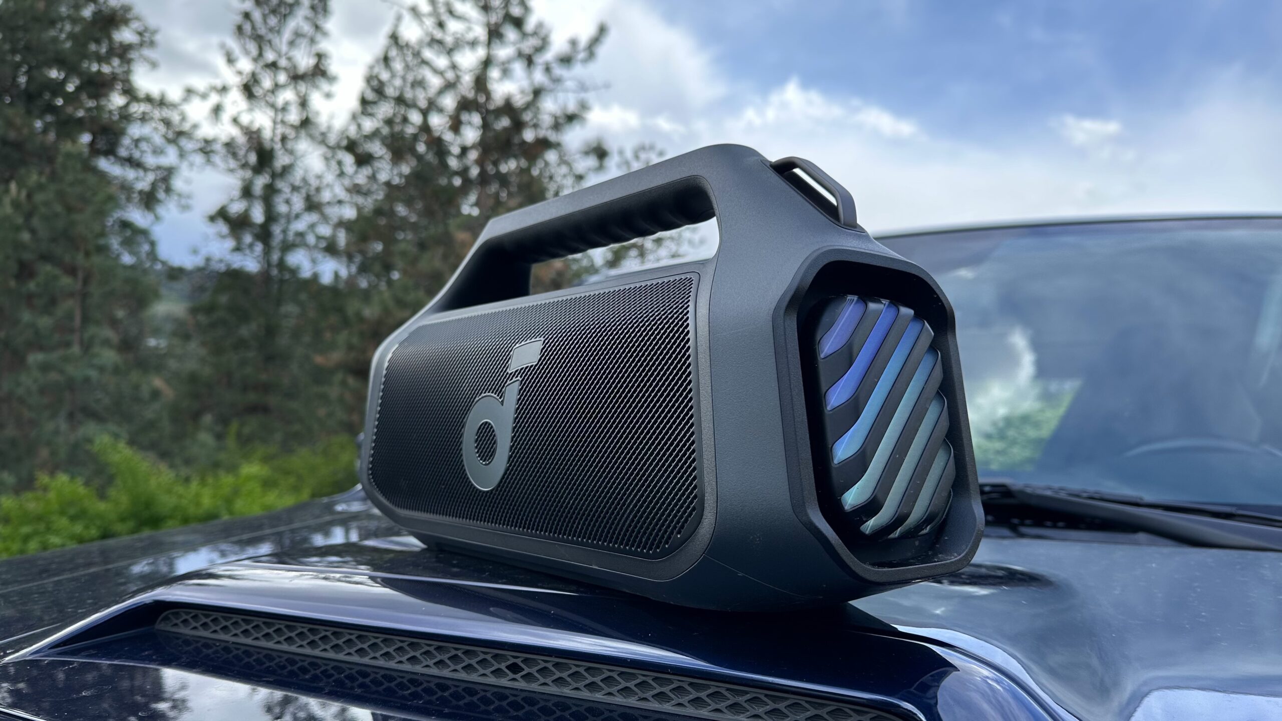 An Anker Soundcore Boom 2 Plus placed on top of an automobile hood, angled towards the camera