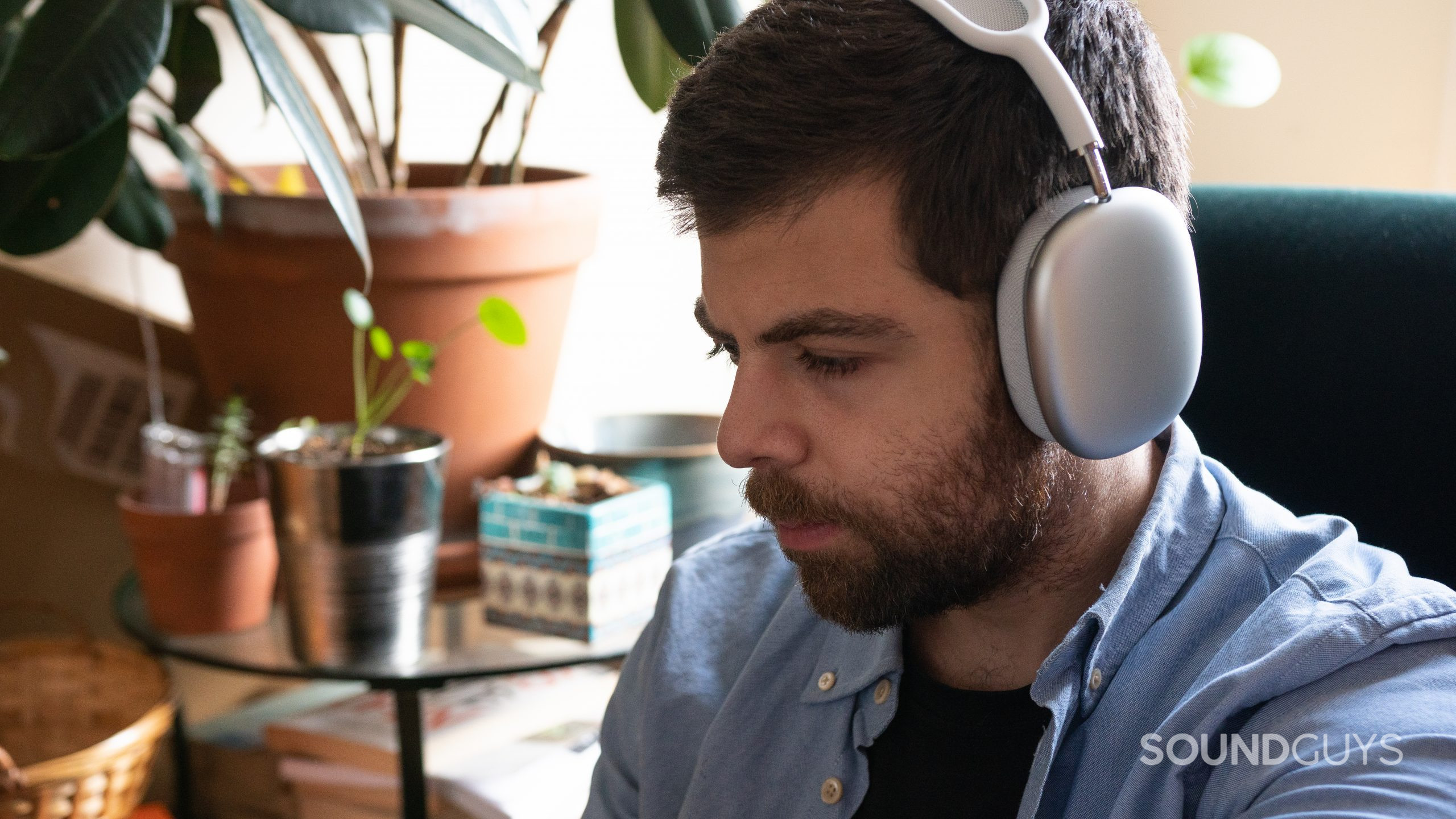 Man wearing the white Apple AirPods Max while sitting in green chair.