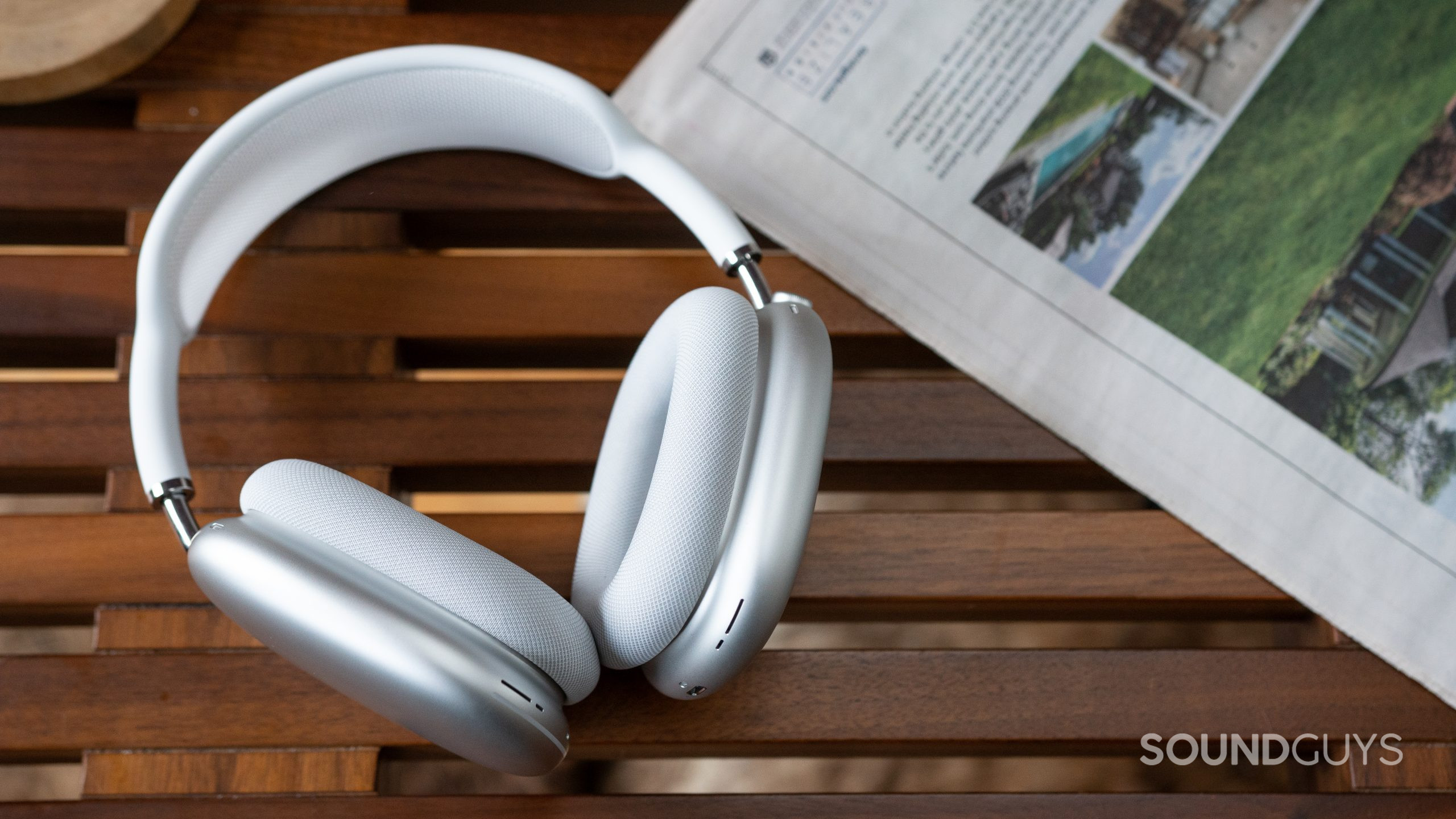 The Apple AirPods Max in white on a coffee table next to a newspaper.