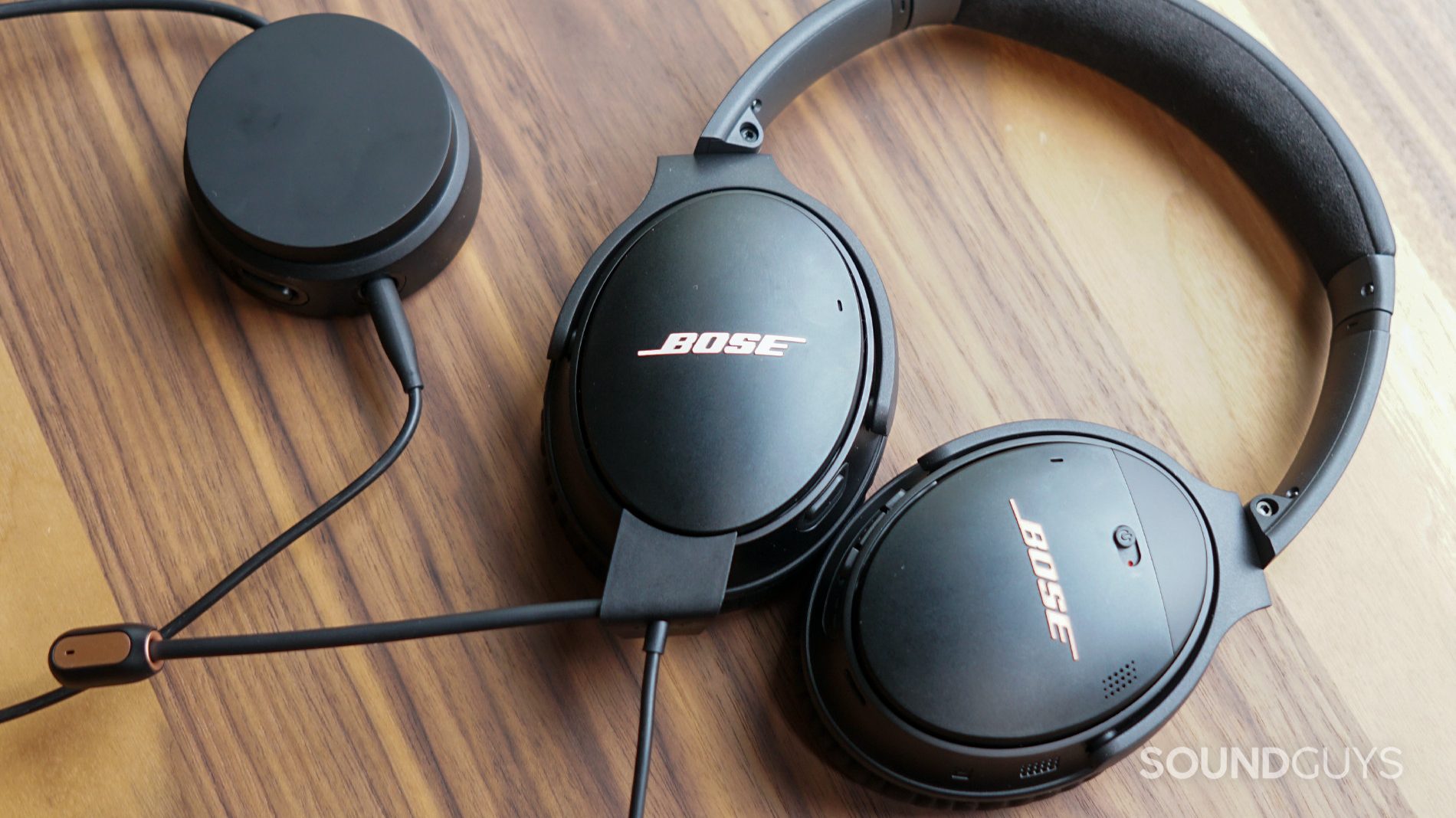 The Bose QuietComfort lays flat on a wooden table plugged into its volume dial.