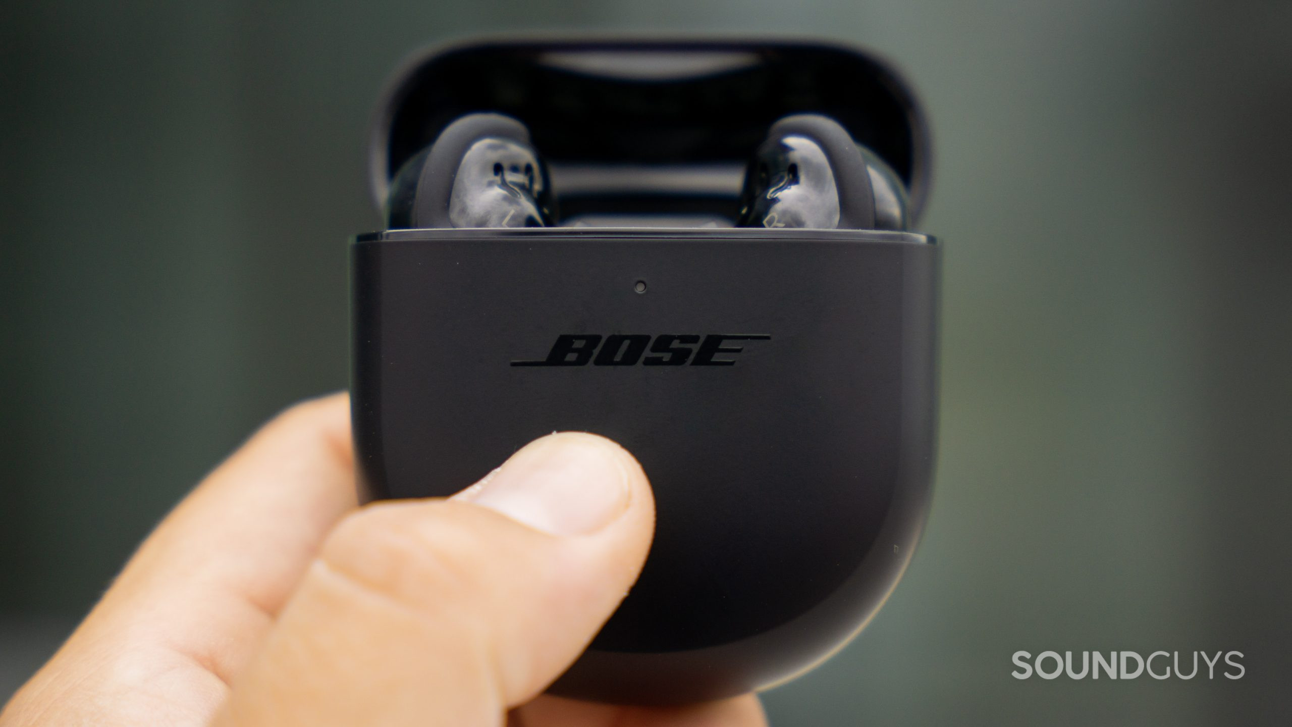 A hand holds the Bose QuietComfort Earbuds II case, which is open and contains the earbuds.