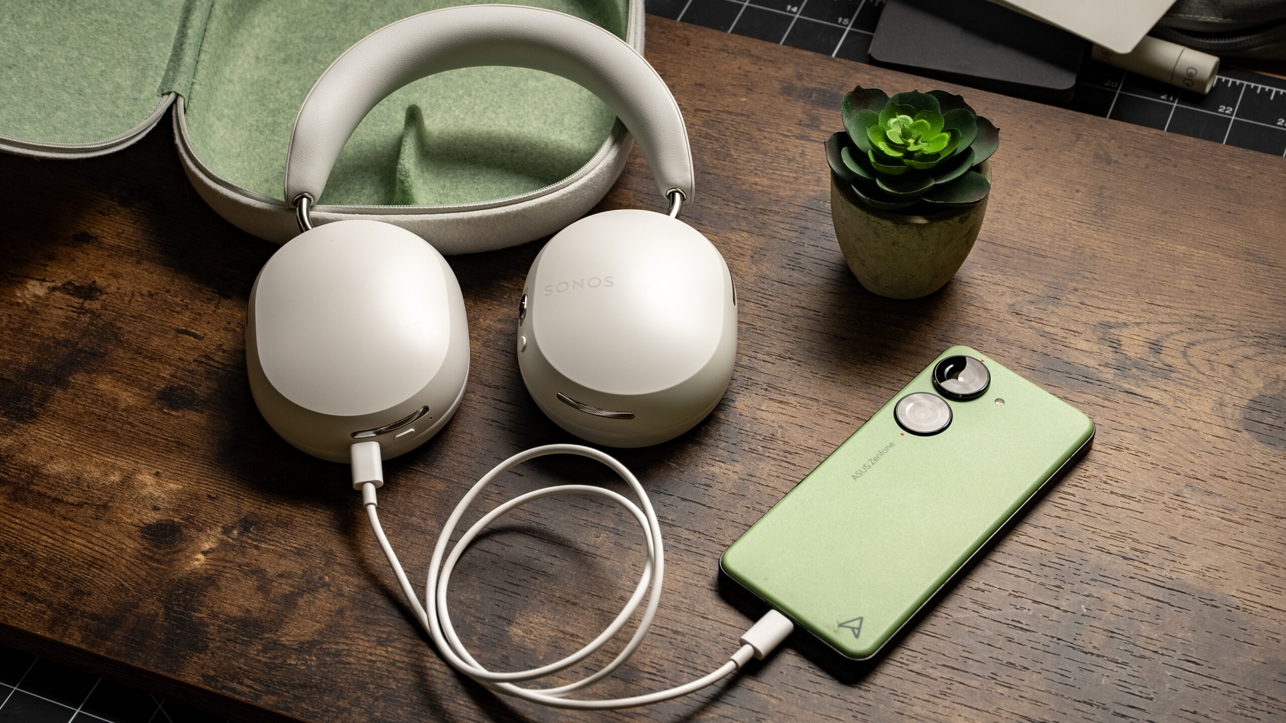 A photo of the Sonos Ace headphones placed against its carrying case conncted to an Android smartphone using a USB-C cable