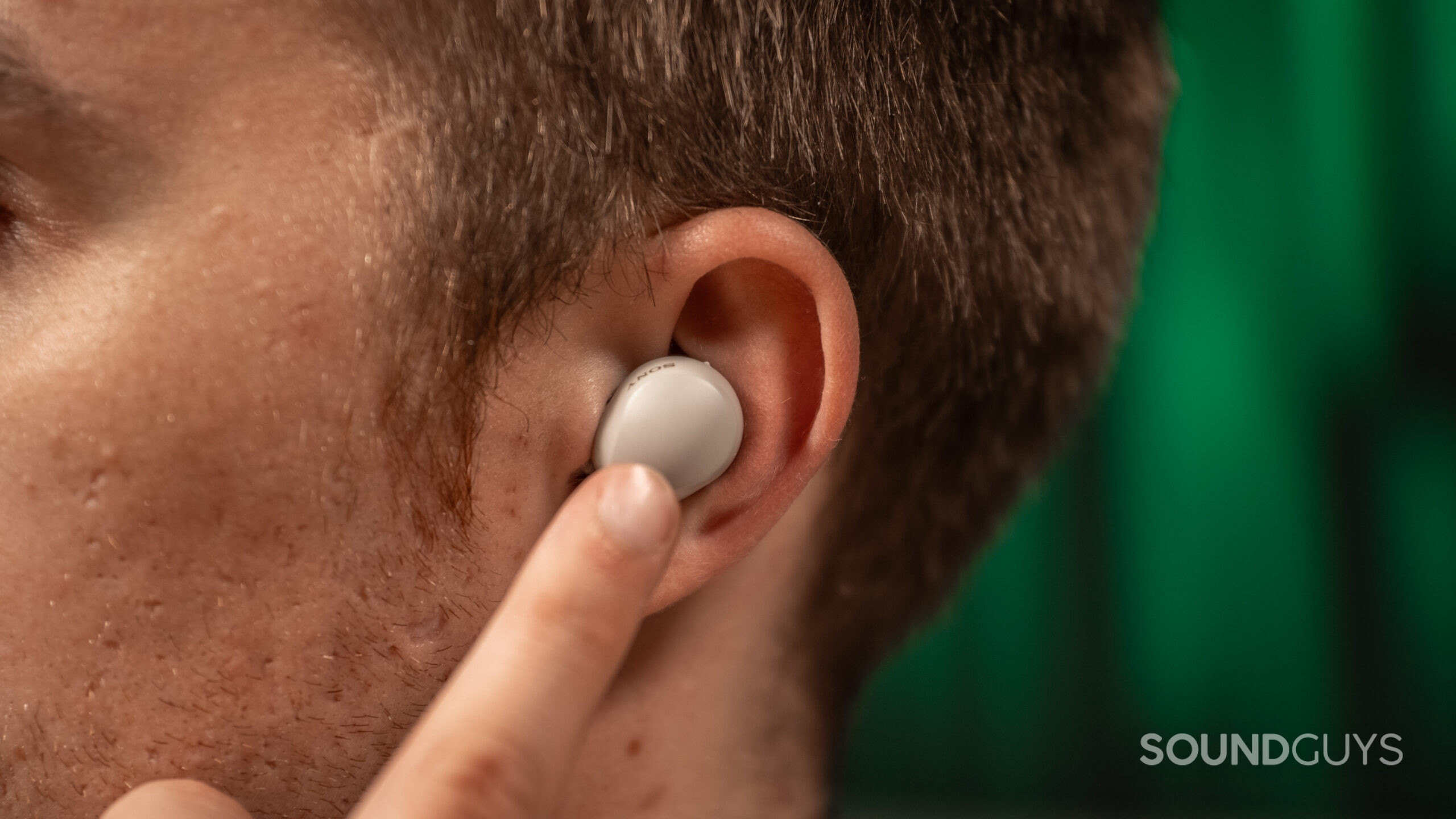 A man wearing the left earbud of the Sony WF-1000XM5 as he holds up a finger to the earbud