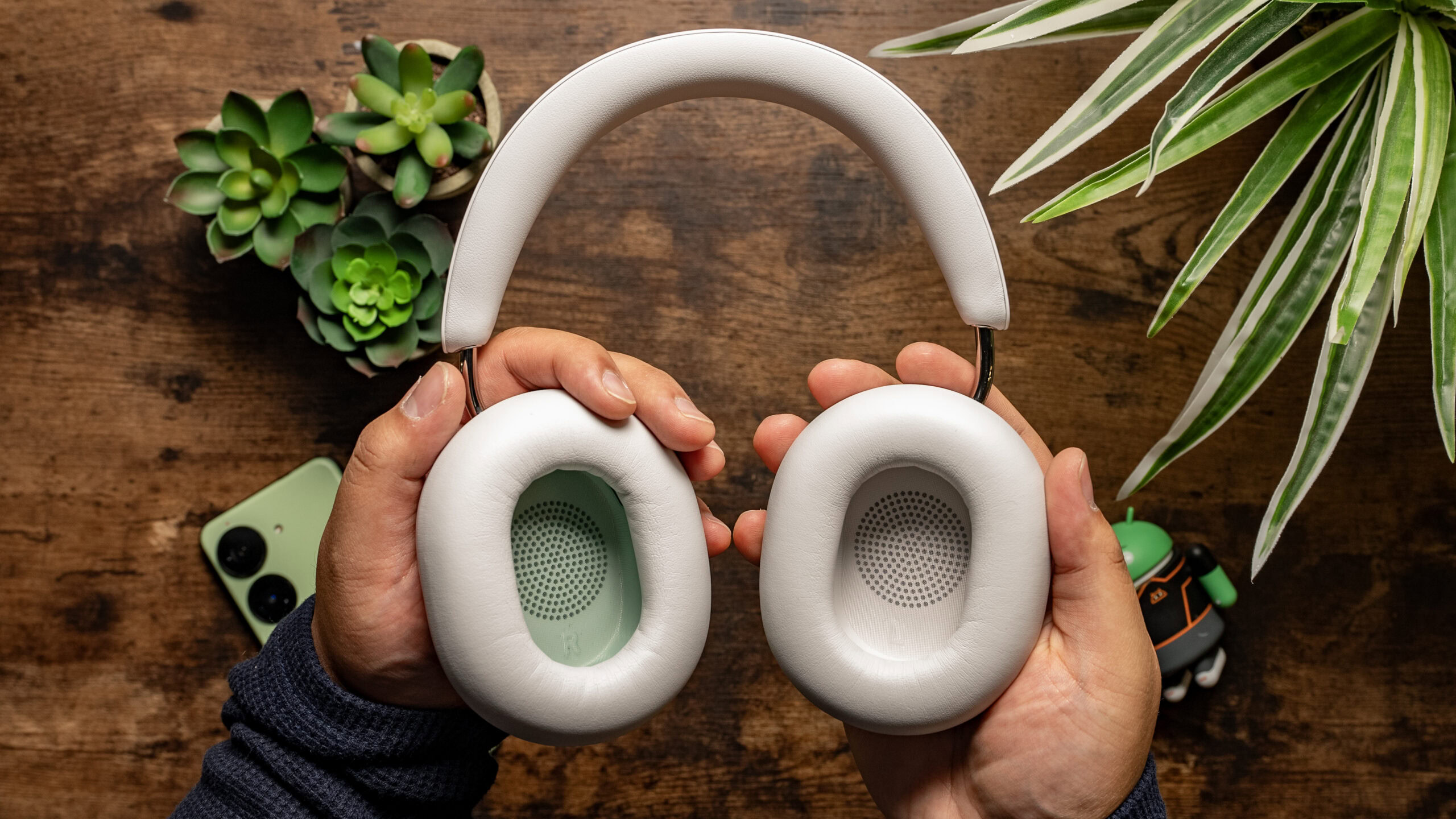 Top down photo of a man holding the Sonos Ace with the ear cups facing outwards to the camera with wooden board background