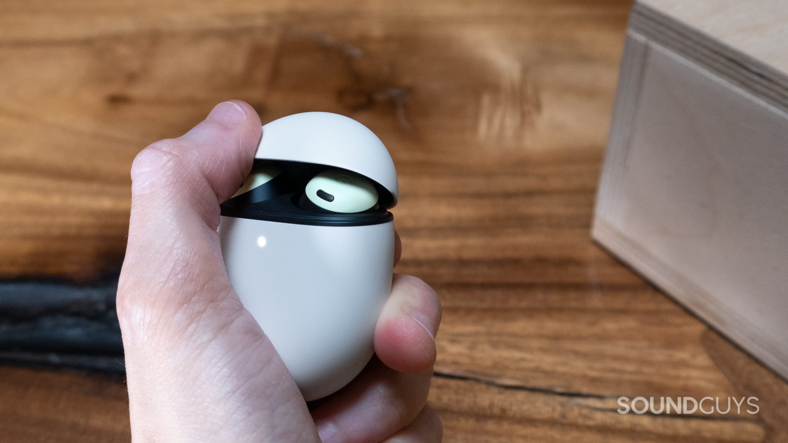 A hand holds the Google Pixel Buds Pro and is in the process of flipping up the lid with a thumb.