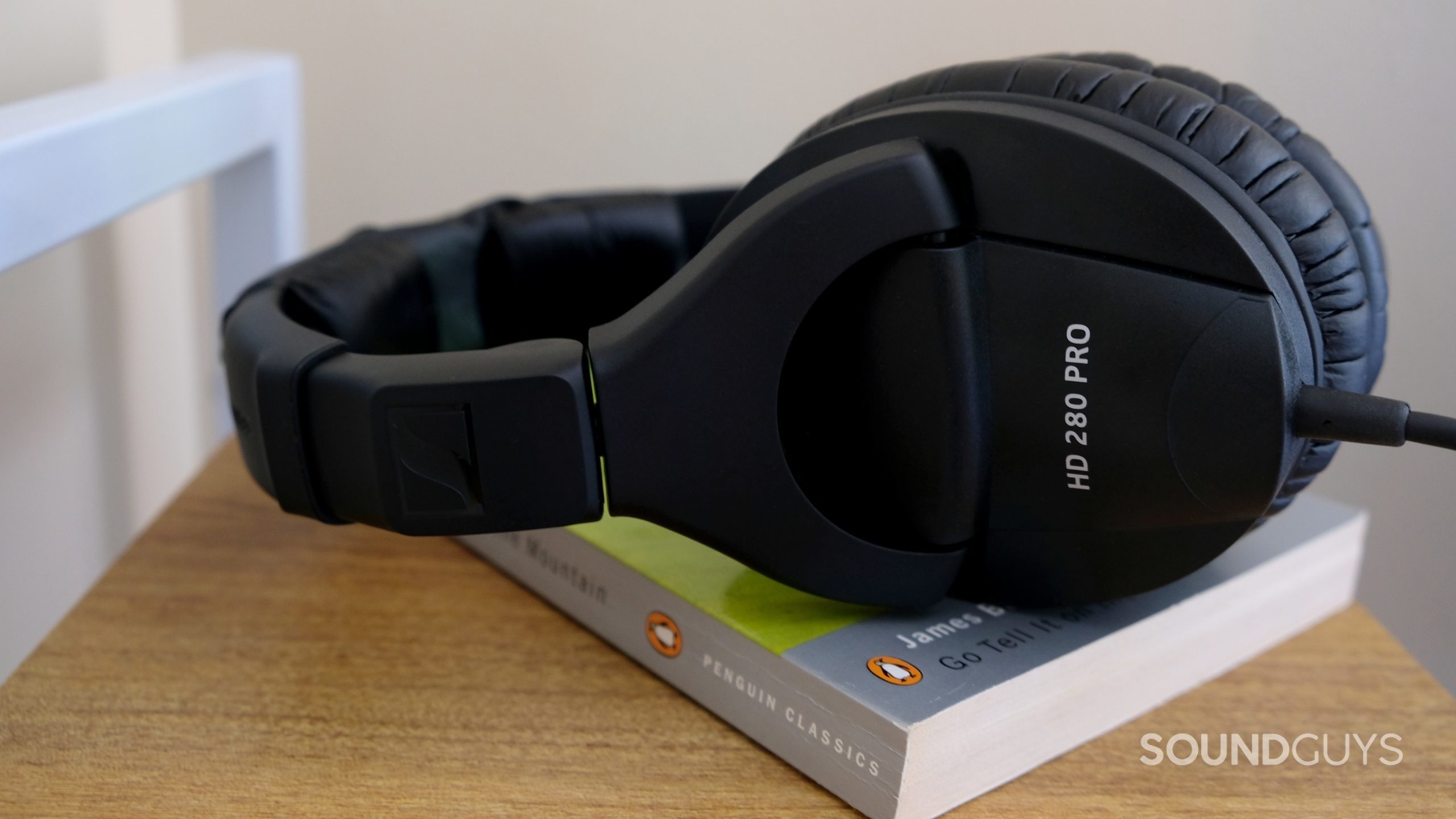 A set of Sennheiser HD 280 Pro sits atop a James Baldwin book on a wood shelf.