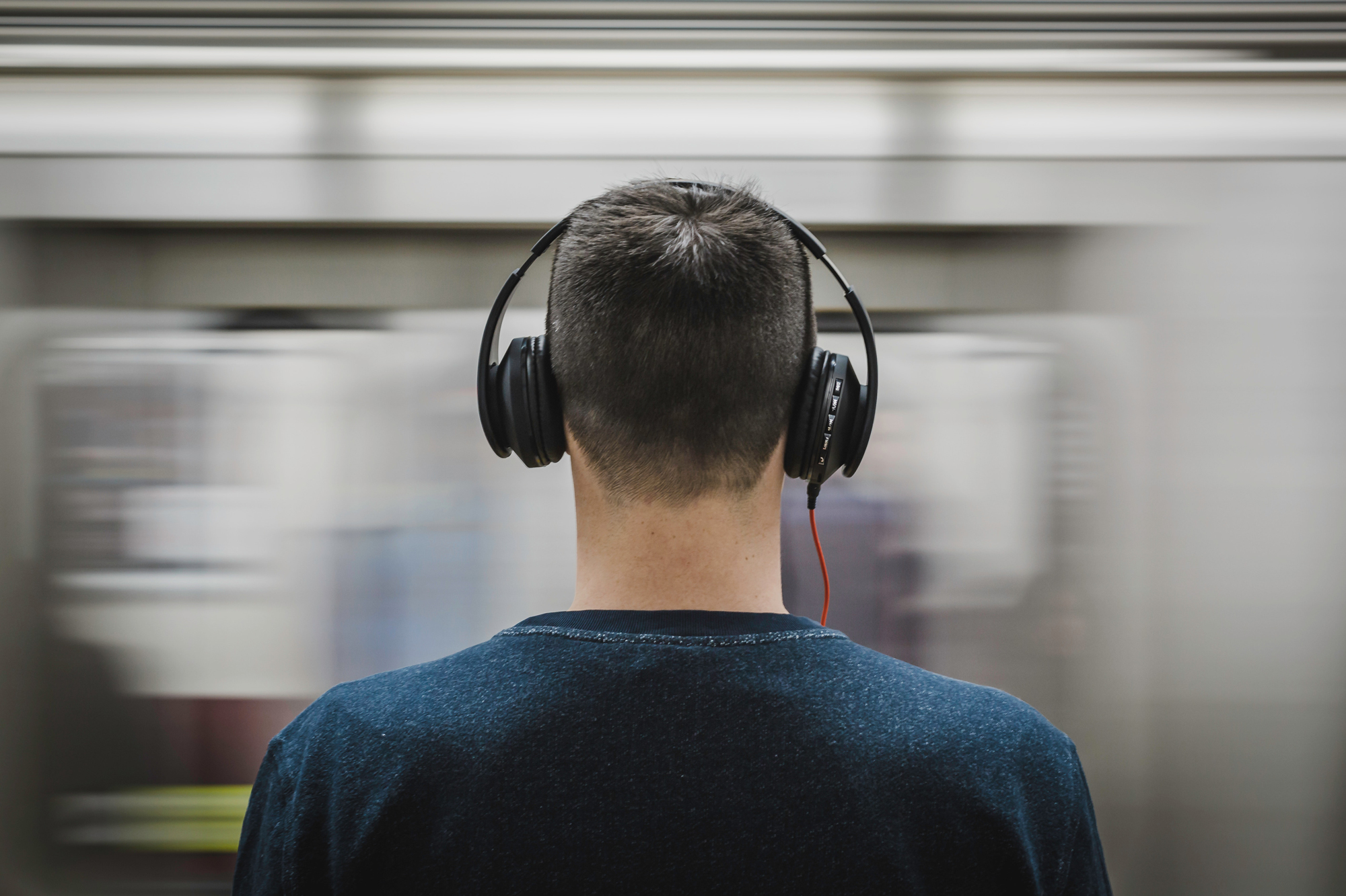 A photo of a young man wearing headphones in front of a moving train, for the article &quot;best headphones for kids.&quot;