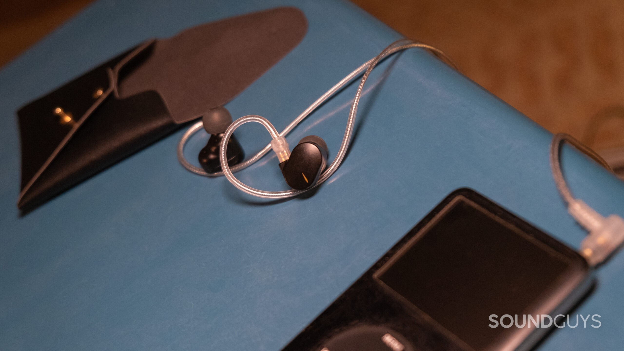 The Moondrop Chu II rests on a blue table with the open carry case in the background and a black iPod in the blurred foreground.