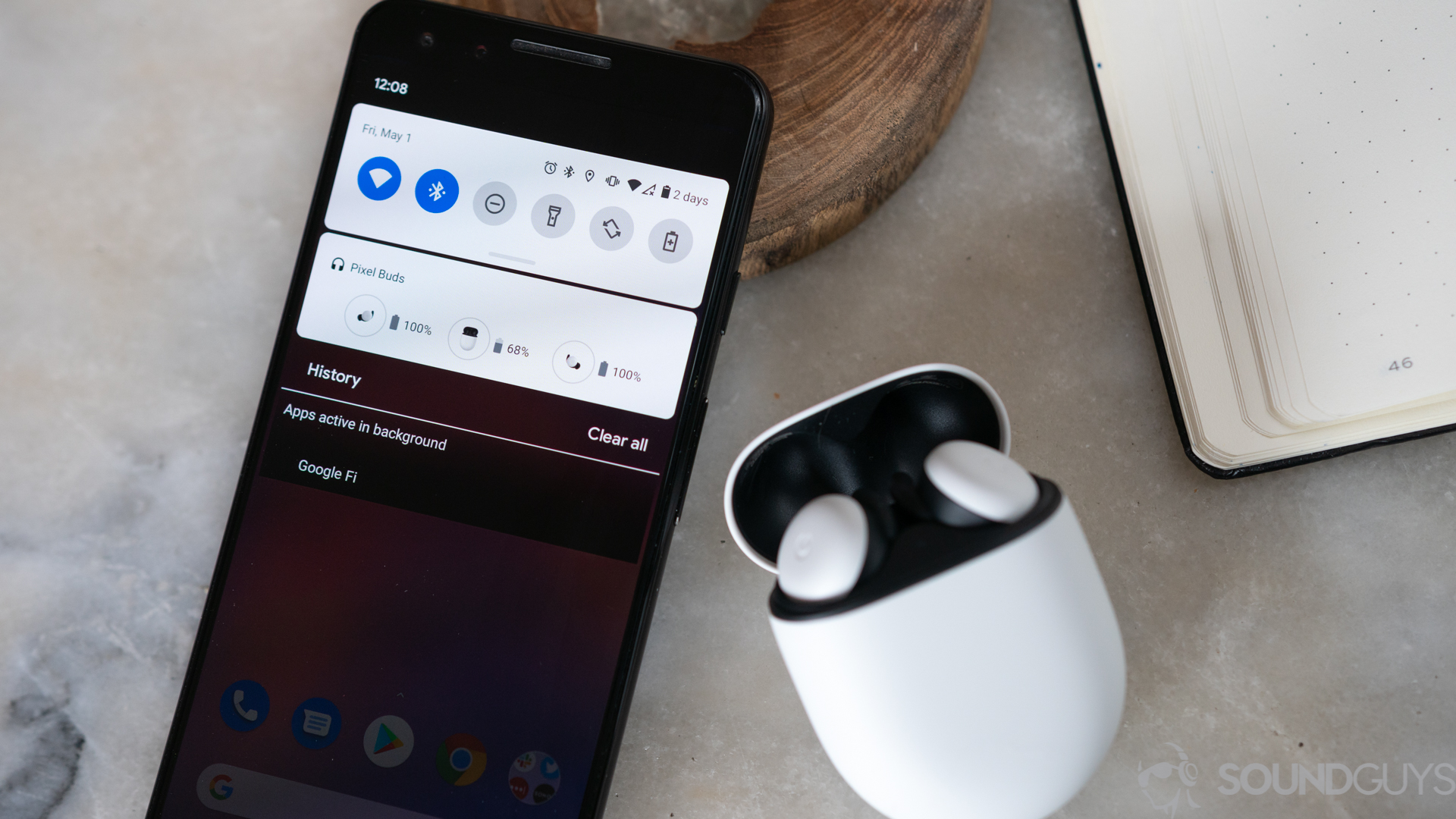 A photo of the white Google Pixel Buds on a marble table next to Pixel 3 with battery card displayed