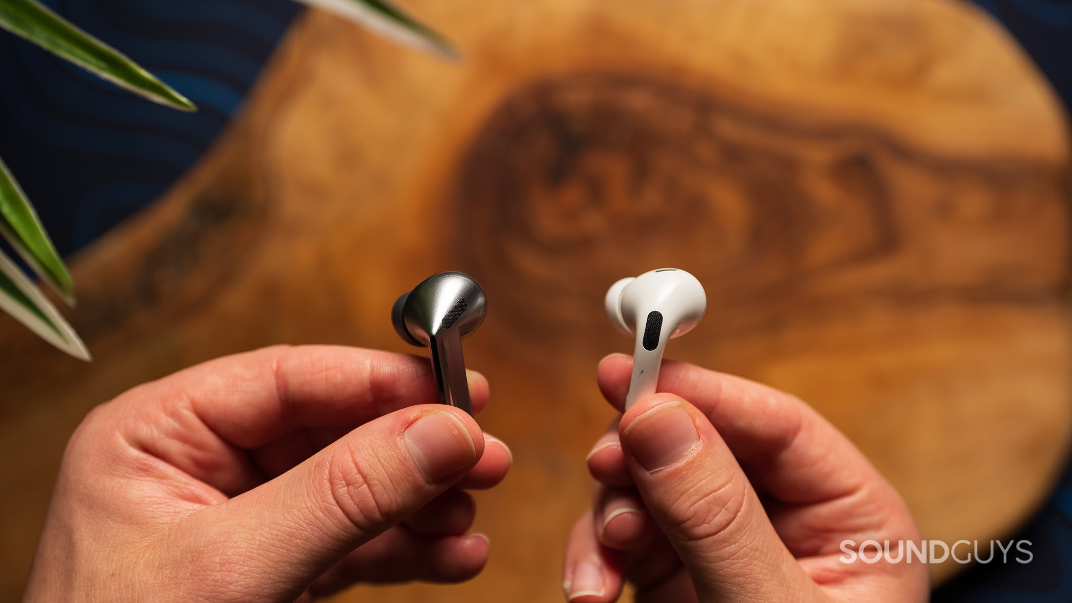 A hand holds a Galaxy Buds3 Pro earbud and a AirPods Pro 2 earbud. 