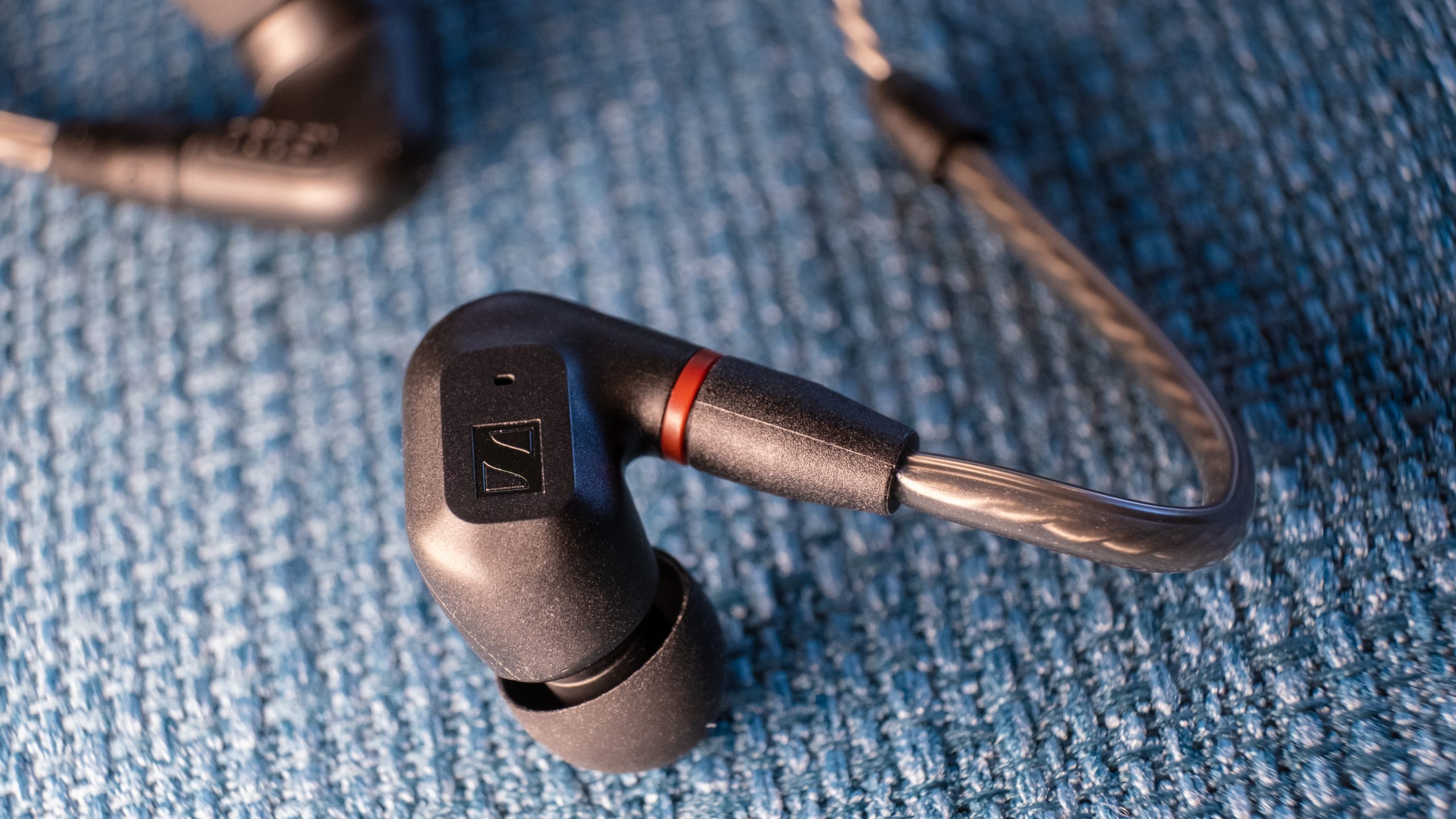 A macro close up of the right Sennheiser IE 200 bud rests on teal fabric.