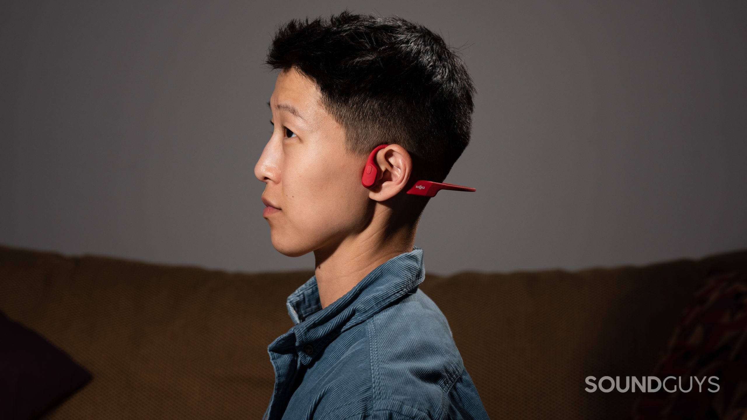 A woman wears the Shokz OpenRun bone conduction headphones in red.