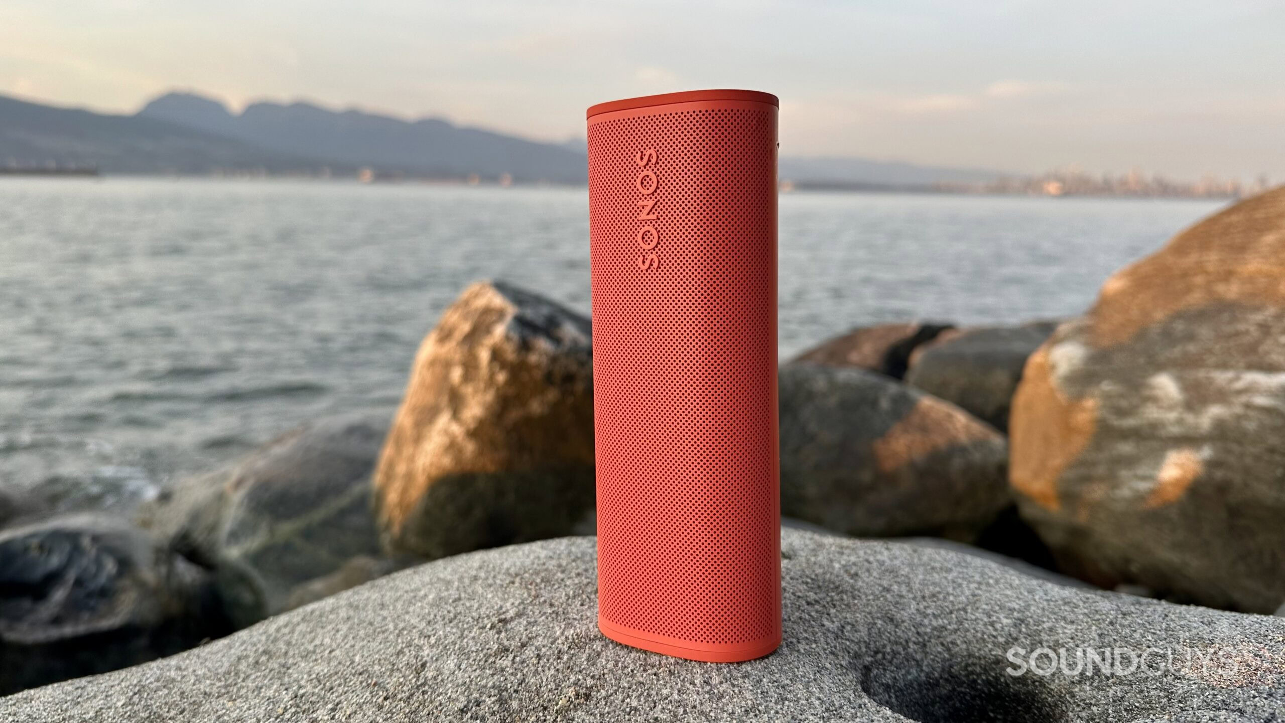 A Sonos Roam 2 placed vertically on a rock near the ocean.