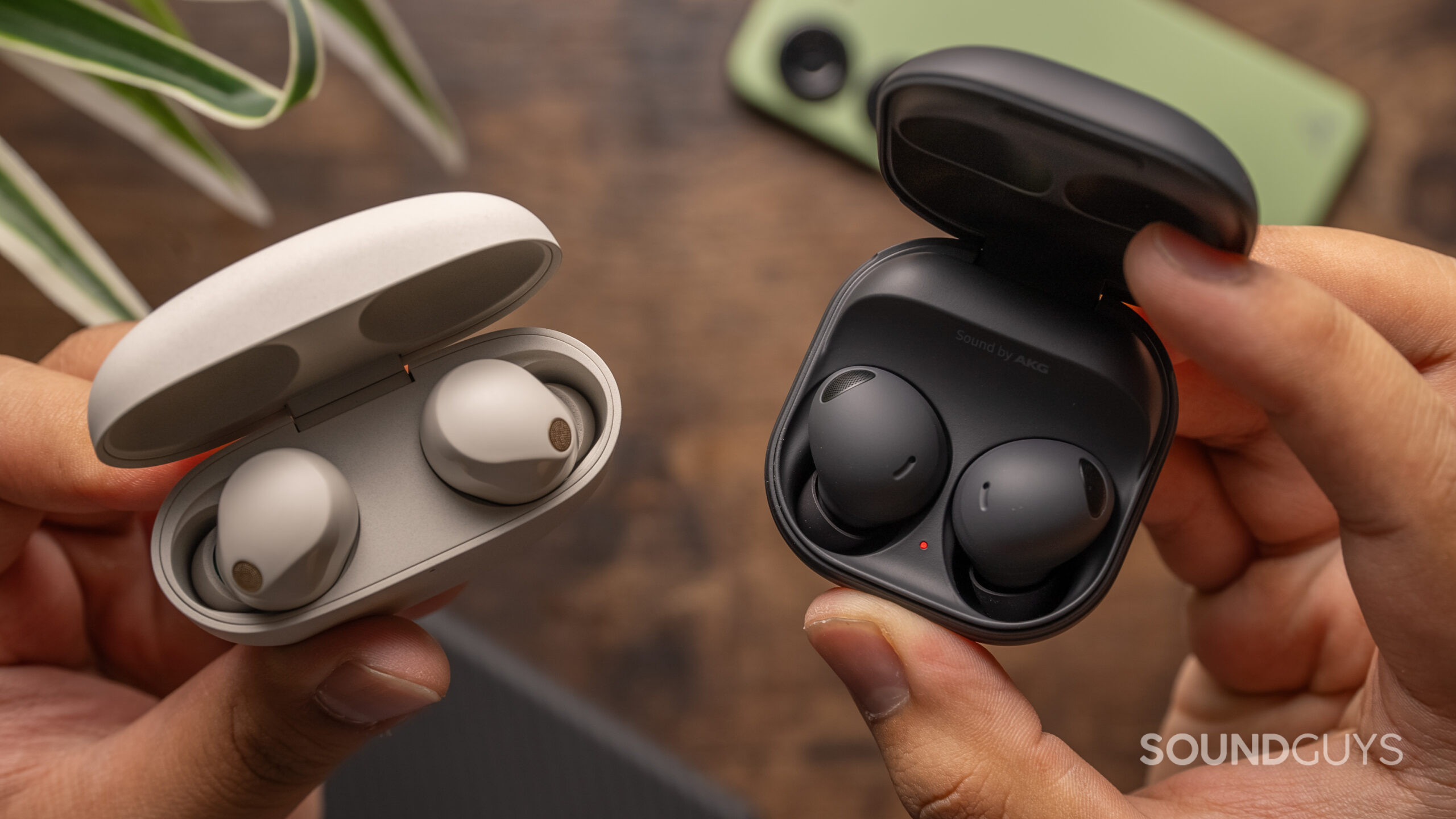 Two hands hold the open cases of the Sony WF-1000XM5 and Samsung Galaxy Buds 2 Pro.