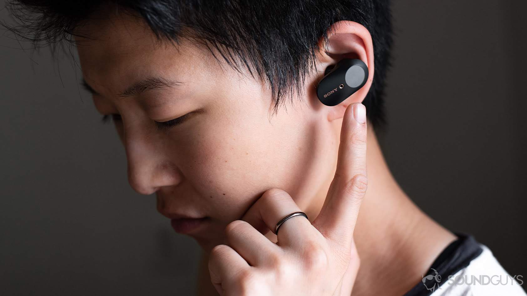 A photo of a woman wearing the Sony WF-1000XM3 earbuds and reaching for the touch panel of the left earbud. Meant to illustrate options for Sony headphones.